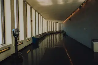 Ilustrasi: Lorong panjang melengkung di dalam gedung dengan deretan jendela besar tanpa orang.