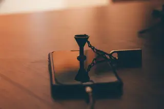 Ilustrasi: Sebuah ponsel pintar dan gantungan flashdisk di atas meja kayu dengan pencahayaan temaram.