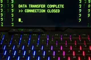 Ilustrasi: Papan ketik dengan lampu latar di depan layar bertuliskan data transfer complete.