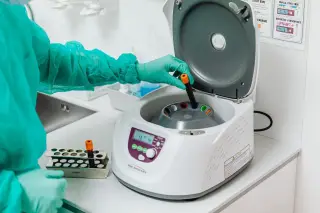 Ilustrasi: Petugas berbaju medis memasukkan tabung sampel ke dalam mesin sentrifugasi di laboratorium.