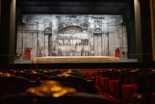 Ilustrasi: Panggung teater kosong berlatar dinding industri dengan jajaran kursi penonton di bagian depan.