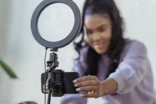Ilustrasi: Seorang wanita menyiapkan ponsel pintar yang terpasang pada tripod dengan lampu ring light.