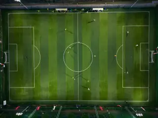 Ilustrasi: Pemandangan dari atas lapangan sepak bola hijau dengan para pemain saat malam hari.