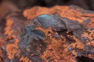 Ilustrasi: Tampilan jarak dekat permukaan batu bijih mineral tambang berwarna gelap dan oranye kecokelatan.