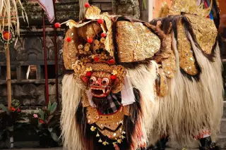 Ilustrasi: Kostum Barong tradisional Bali dengan hiasan emas dan bulu lebat di pelataran pura.