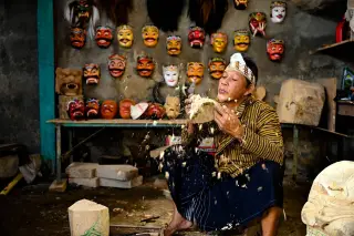 Ilustrasi: Seorang pria mengenakan pakaian tradisional meniup serpihan kayu saat mengukir topeng tradisional.
