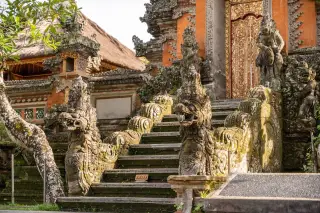 Ilustrasi: Tangga batu berukir patung naga dan arca menuju pintu gerbang pura bergaya Bali.
