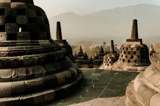 Ilustrasi: Deretan stupa Candi Borobudur dengan latar belakang pemandangan perbukitan berkabut.
