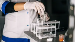 Ilustrasi: Petugas bersarung tangan memegang tabung reaksi di rak laboratorium.