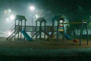 Ilustrasi: Area bermain anak yang sepi di malam hari diselimuti kabut tebal di bawah cahaya lampu taman.