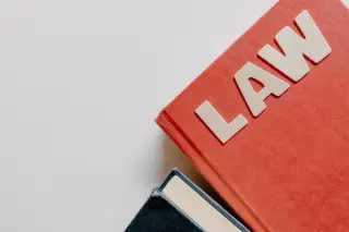 Ilustrasi: Buku merah bertuliskan LAW dan buku hitam di atas latar belakang putih.