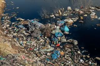 Ilustrasi: Tumpukan sampah plastik dan limbah mengotori tepi aliran air yang keruh.