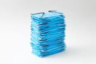Ilustrasi: Tumpukan masker medis berwarna biru dengan latar belakang putih polos.
