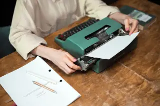 Ilustrasi: Seseorang sedang mengetik naskah menggunakan mesin tik manual di atas meja kayu.