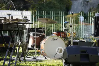 Ilustrasi: Satu set drum dan instrumen musik tertata di atas rumput di depan pagar besi.