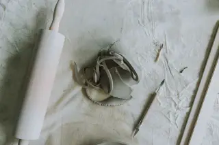 Ilustrasi: Potongan tanah liat dan alat ukir serta penggiling kayu di atas kain meja kerja.