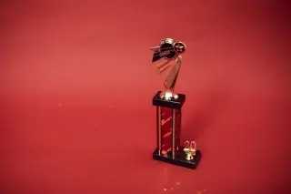 Ilustrasi: Sebuah piala penghargaan berwarna emas berdiri di atas latar belakang merah polos.