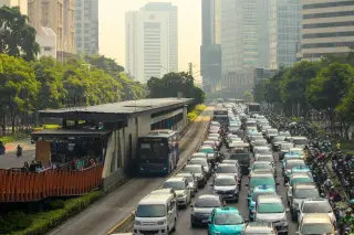 Ilustrasi: Kemacetan lalu lintas mobil, bus, dan motor di jalan raya berlatar gedung bertingkat.