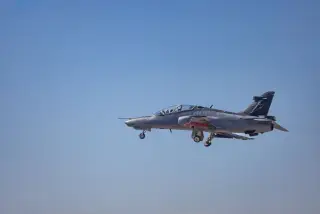 Ilustrasi: Sebuah pesawat tempur latih militer terbang di langit biru dengan roda pendaratan terbuka.