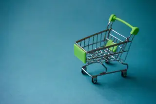 Ilustrasi: Troli belanja miniatur beraksen hijau di atas latar belakang biru polos.