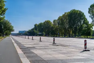 Ilustrasi: Deretan patok pembatas lalu lintas bergaris merah putih di area jalanan beraspal yang luas dan lengang.