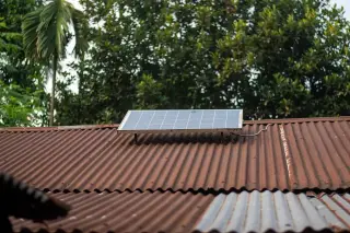 Ilustrasi: Satu panel surya kecil terpasang di atas atap seng berkarat dengan latar pepohonan rimbun.