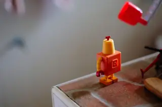 Ilustrasi: Mainan robot kecil berwarna oranye berdiri di atas permukaan meja.