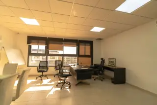 Ilustrasi: Ruangan kantor kosong dengan meja kerja, kursi putar, dan jendela berpemandangan bangunan luar.