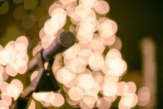 Ilustrasi: Mikrofon panggung dengan latar belakang efek bokeh lampu hangat yang buram.