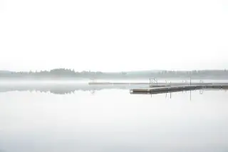 Ilustrasi: Dermaga kayu terapung di danau tenang yang diselimuti kabut tebal dan deretan pepohonan di kejauhan.