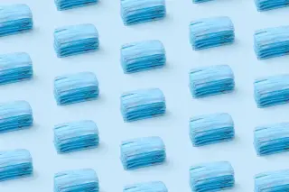 Ilustrasi: Pola tumpukan masker medis berwarna biru yang tersusun rapi di atas latar belakang biru muda.