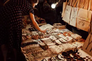 Ilustrasi: Seorang wanita melihat aneka produk kerajinan tangan dan tas kain di sebuah bazar malam.