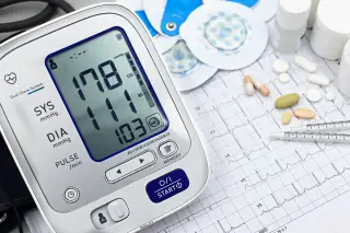 Ilustrasi: Tensimeter digital, hasil cetak EKG, dan obat-obatan di atas meja.