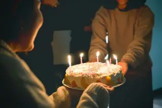 Ilustrasi: Seseorang memegang kue ulang tahun dengan lilin-lilin menyala di hadapan orang lain.