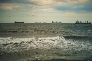 Ilustrasi: Sejumlah kapal kargo dan tanker melintas di laut lepas dengan ombak berbusa di latar depan.