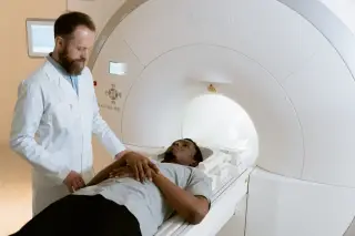Ilustrasi: Seorang dokter berdiri di samping pasien yang berbaring di mesin pemindai medis.