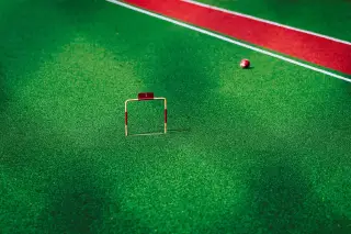 Ilustrasi: Gawang kecil dan bola gateball di atas lapangan rumput sintetis hijau.