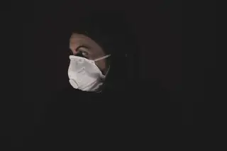 Ilustrasi: Seorang wanita mengenakan masker respirator putih dengan latar belakang hitam gelap.