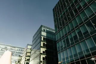 Ilustrasi: Deretan gedung perkantoran modern berdinding kaca di bawah langit biru cerah.
