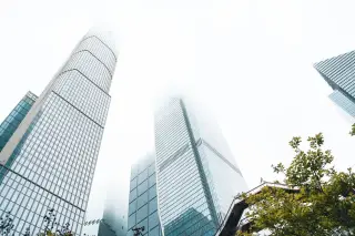 Ilustrasi: Pemandangan gedung pencakar langit modern berbalut kabut dari sudut rendah.