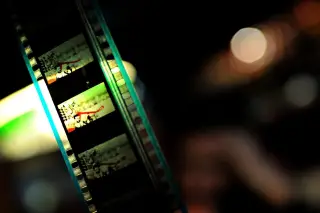 Ilustrasi: Potongan pita film seluloid dengan latar belakang gelap dan efek bokeh bercahaya.