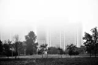 Ilustrasi: Foto hitam putih gedung-gedung bertingkat yang terselimuti kabut tebal di balik taman kota.