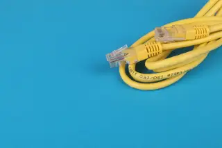 Ilustrasi: Gulungan kabel jaringan ethernet berwarna kuning dengan konektor di atas latar belakang biru.