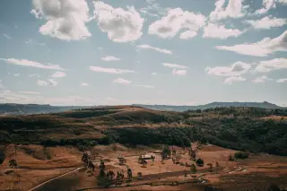 Ilustrasi: Pemandangan perbukitan savana kecokelatan di bawah langit berawan.