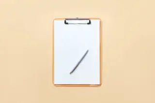 Ilustrasi: Papan klip dengan selembar kertas putih kosong dan sebuah pulpen di atas permukaan krem.