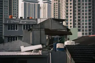 Ilustrasi: Atap-atap rumah perkotaan berlatar belakang deretan gedung apartemen tinggi.