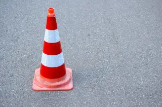Ilustrasi: Sebuah kerucut lalu lintas berwarna oranye dan putih berdiri di atas aspal jalan.