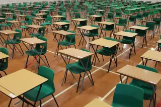 Ilustrasi: Deretan meja dan kursi lipat kosong tersusun rapi di dalam aula berlantai kayu.