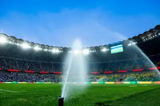Ilustrasi: Penyiram air menyemprotkan air ke lapangan rumput stadion sepak bola besar di bawah lampu sorot.