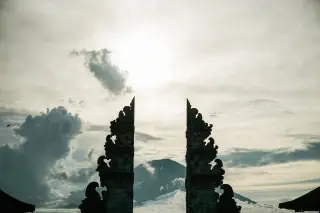 Ilustrasi: Siluet gerbang pura berlatar belakang gunung dan langit berawan di Bali.